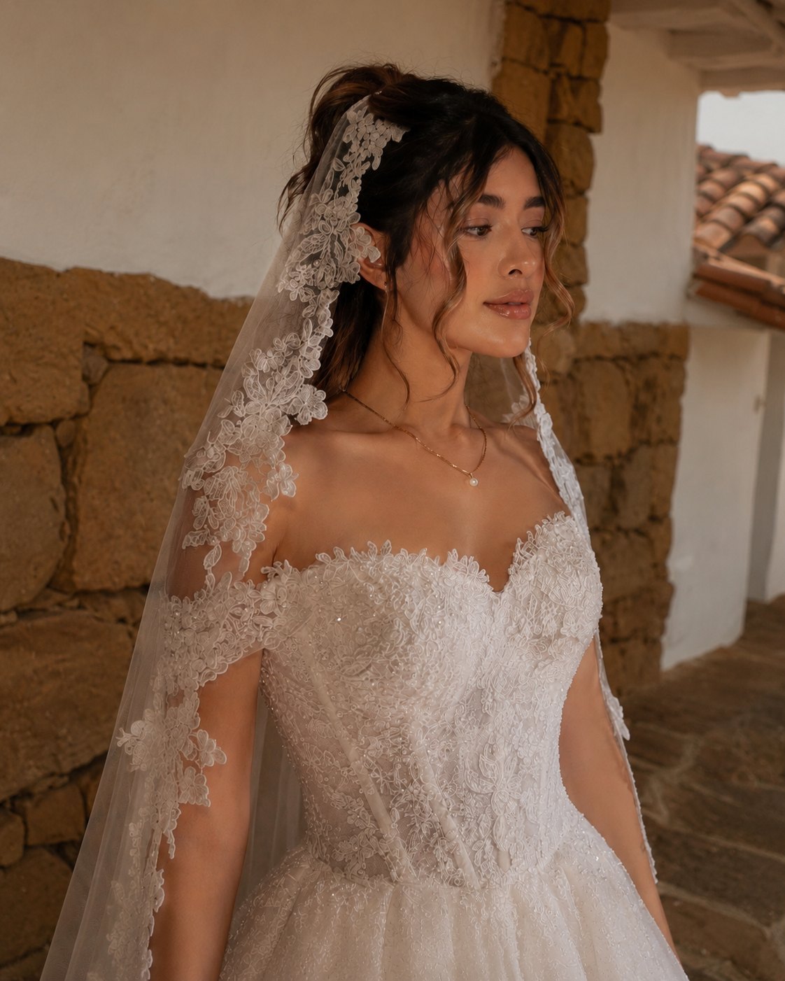 Novia con velo de encaje junto a un muro de piedra